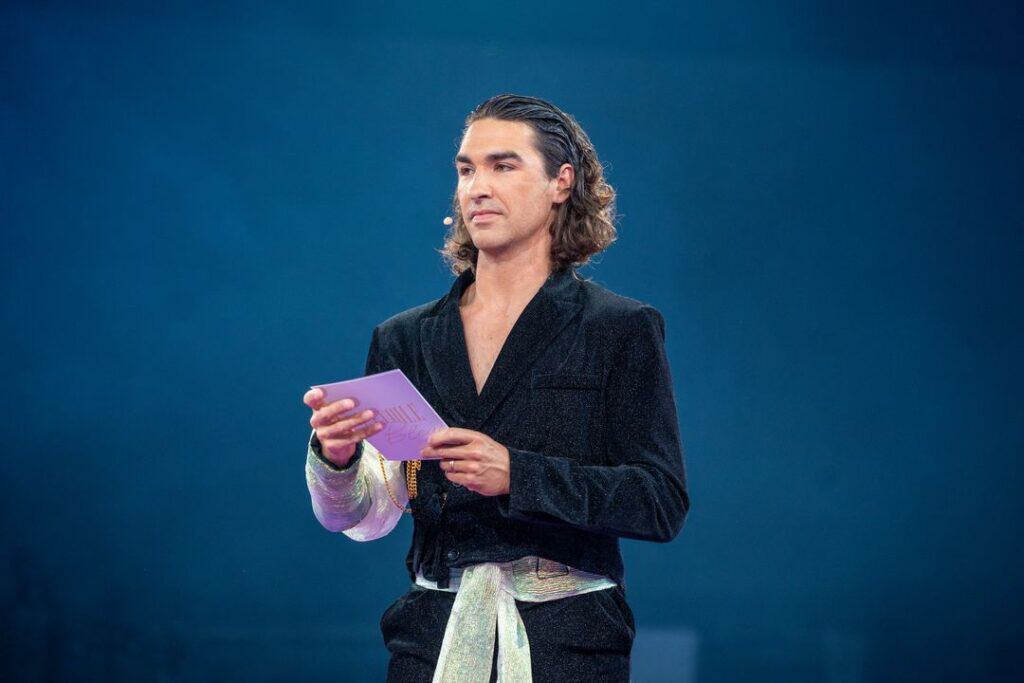 Homme en costume noir lisant un script lors d'une performance au cabaret.